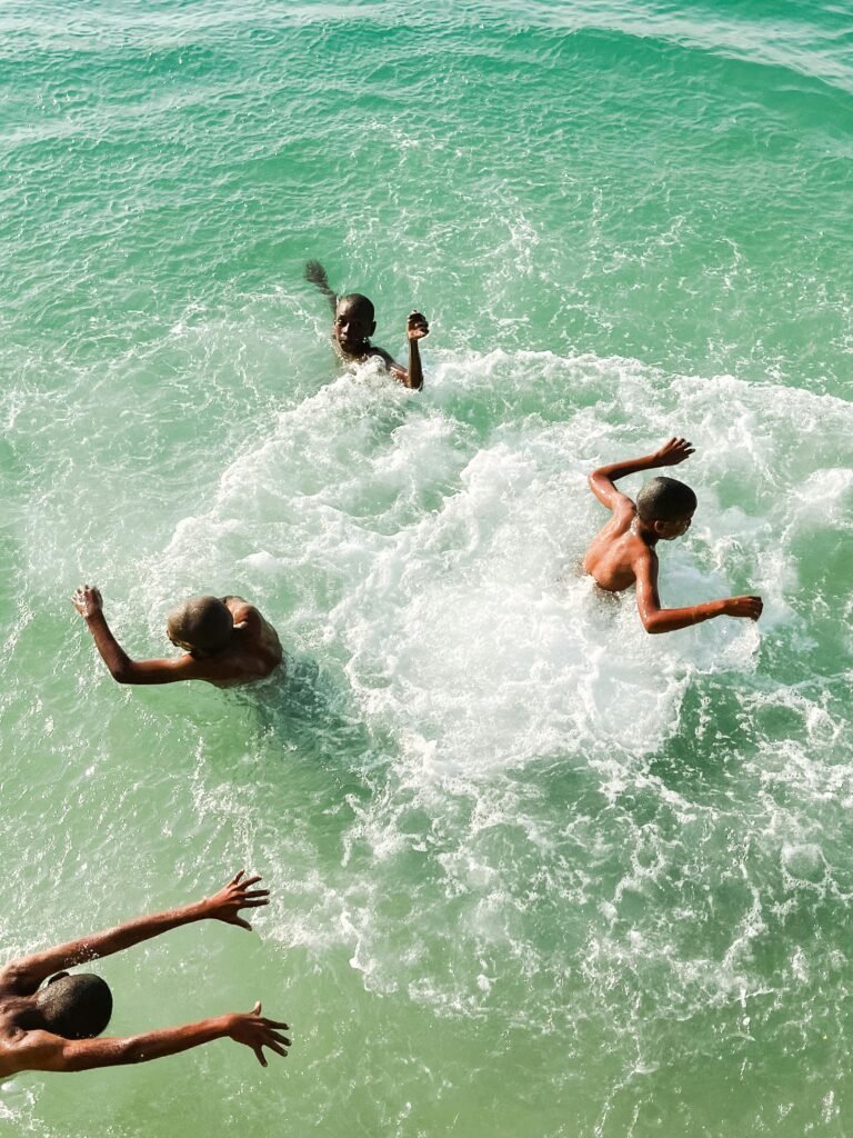 Young boys swimming and playing in the clear ocean waters of Tanzania under a bright sunny day.