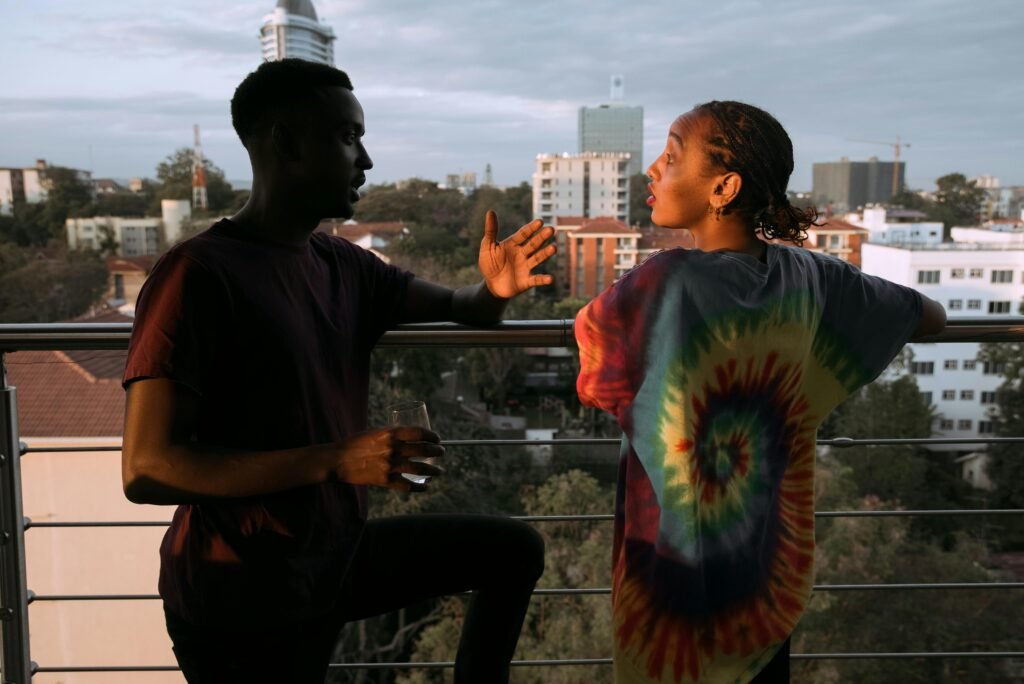 A couple in vibrant attire engaged in conversation on a city balcony at sunset.